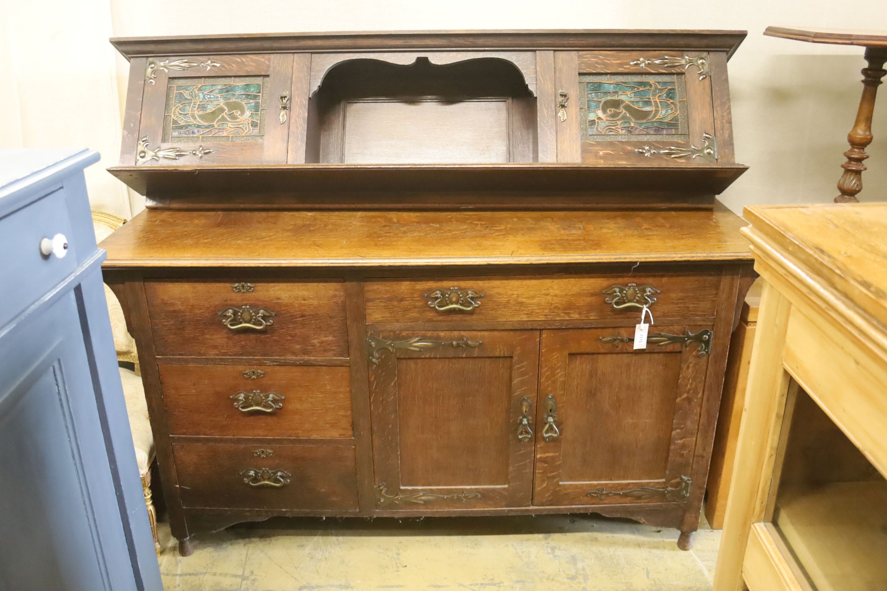 An Arts & Crafts style oak sideboard with stained glass dolphin panels, length 182cm, depth 60cm, height 145cm (lacks top section suppo